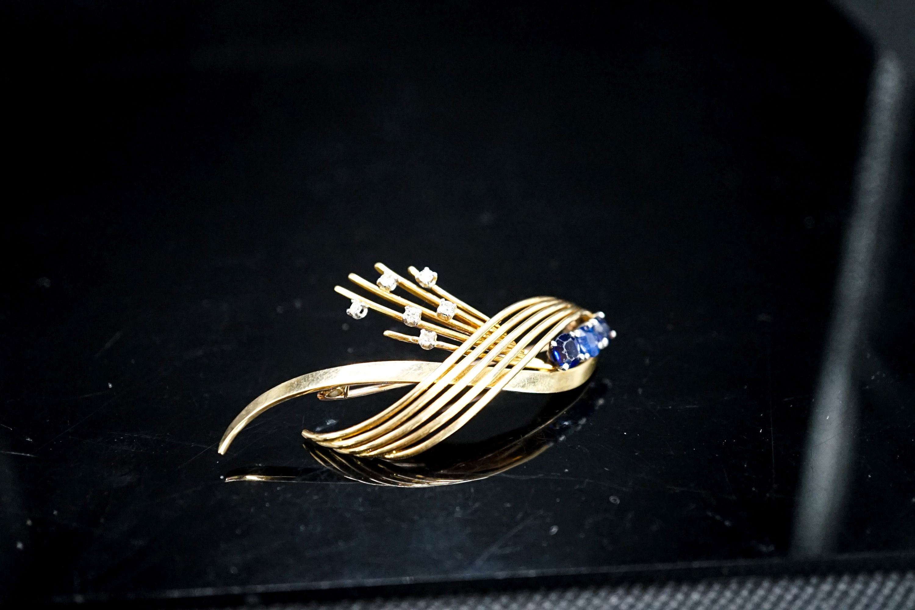 A modern yellow metal, sapphire and diamond set stylised spray brooch, 53mm, gross 9.7 grams.